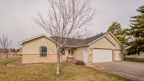 A two-story house with a garage, a front yard with a small tree, and a driveway.