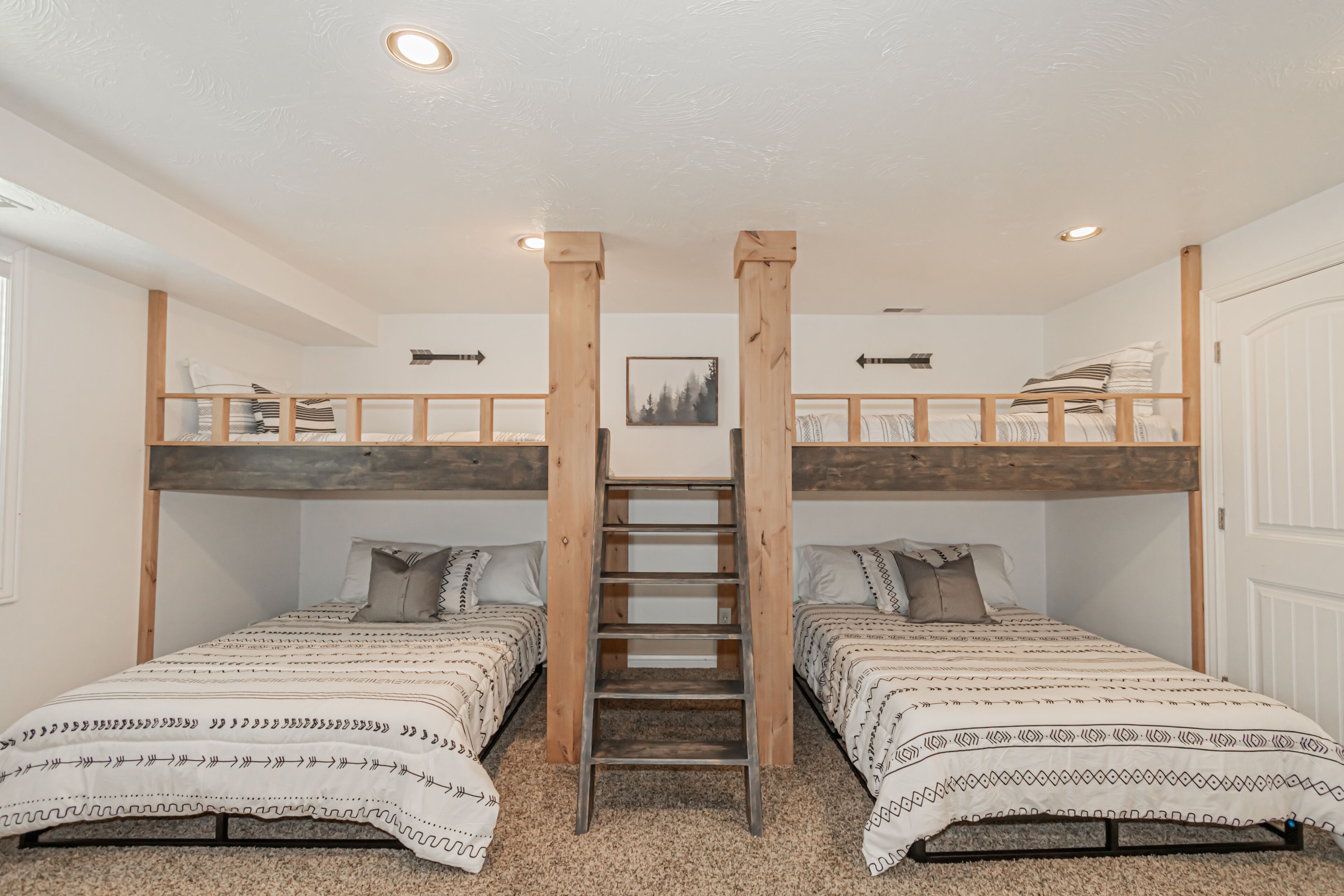 A room with two bunk beds, a ladder, and a framed picture on the wall.
