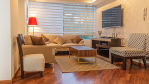 Una sala de estar moderna con sofá, reposapiés, mesa de centro, sillón estampado y un televisor de pantalla plana montado en la pared.