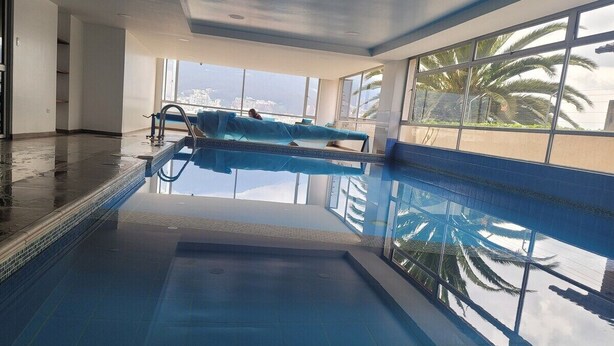 Piscina interior con vistas a palmeras y al paisaje urbano a través de amplias ventanas.