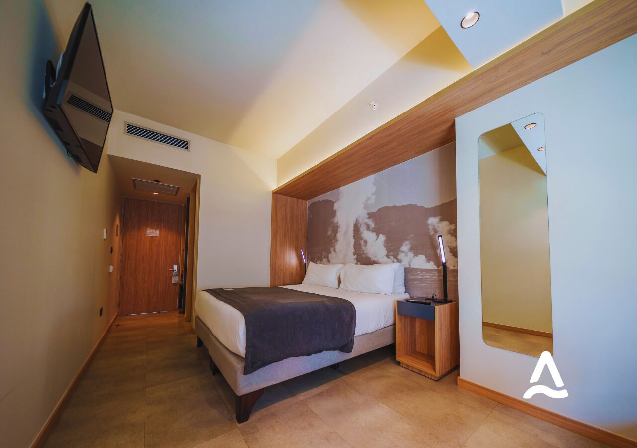 Een moderne hotelkamer met een bed, nachtkastje en een grote spiegel.