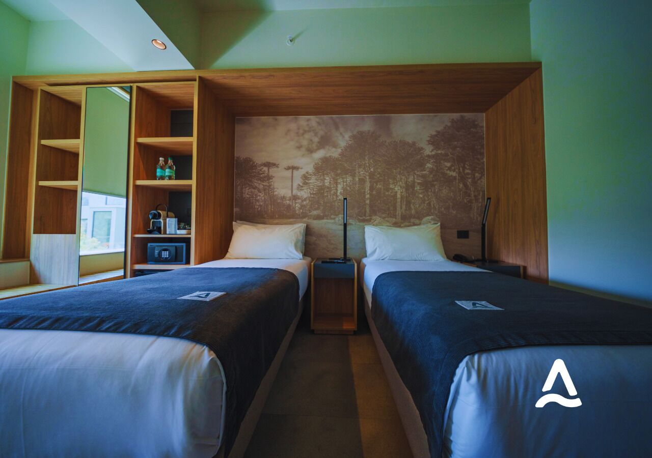 A hotel room with two beds, a wooden wardrobe, a small desk, and a large mirror.