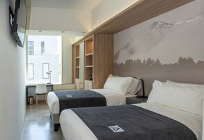 Habitación de hotel con dos camas, un escritorio, una silla, un televisor y un mural con vistas a la montaña.
