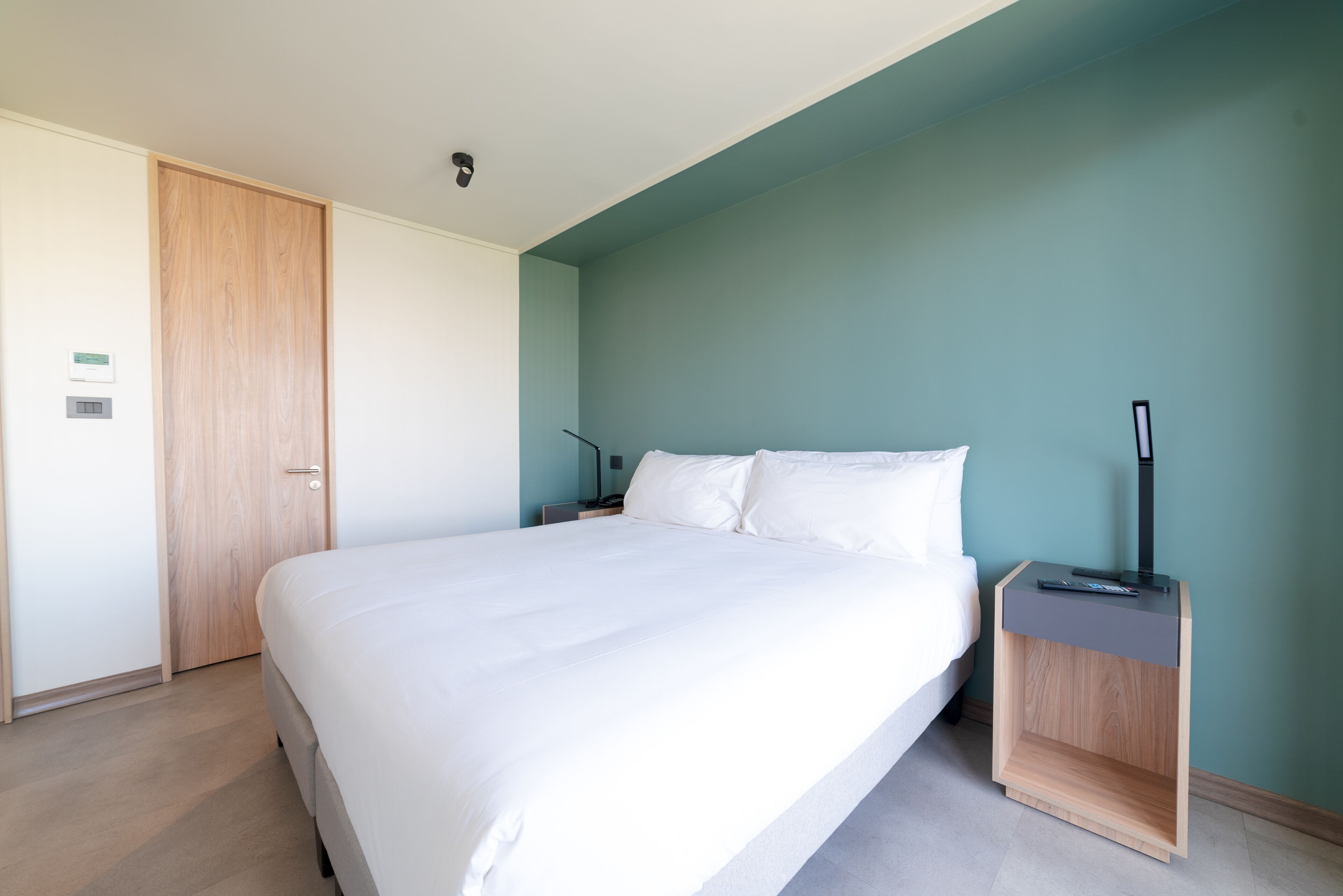 A neatly made bed in a room with a wooden door and a nightstand with a lamp.
