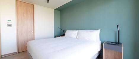 A neatly made bed in a room with a wooden door and a nightstand with a lamp.