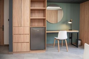 Ein kleines Zimmer mit eingebautem Holzschrank, einem Schreibtisch mit Stuhl und einem runden Spiegel an der Wand.