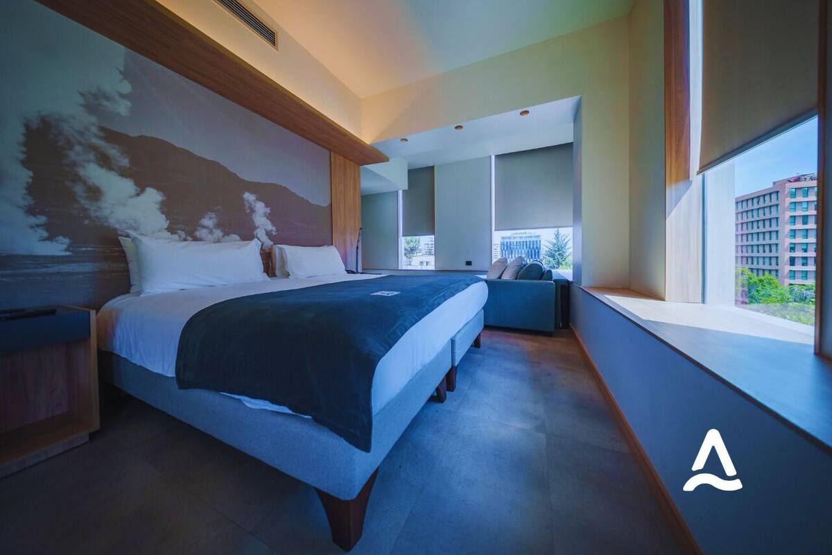 Een moderne hotelkamer met een groot bed, een zithoek en uitzicht op de stad door grote ramen.