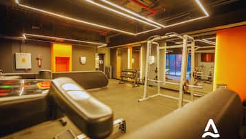 Un gimnasio con equipo de ejercicio, un rack de pesas y vistas de la ciudad a través de grandes ventanales.