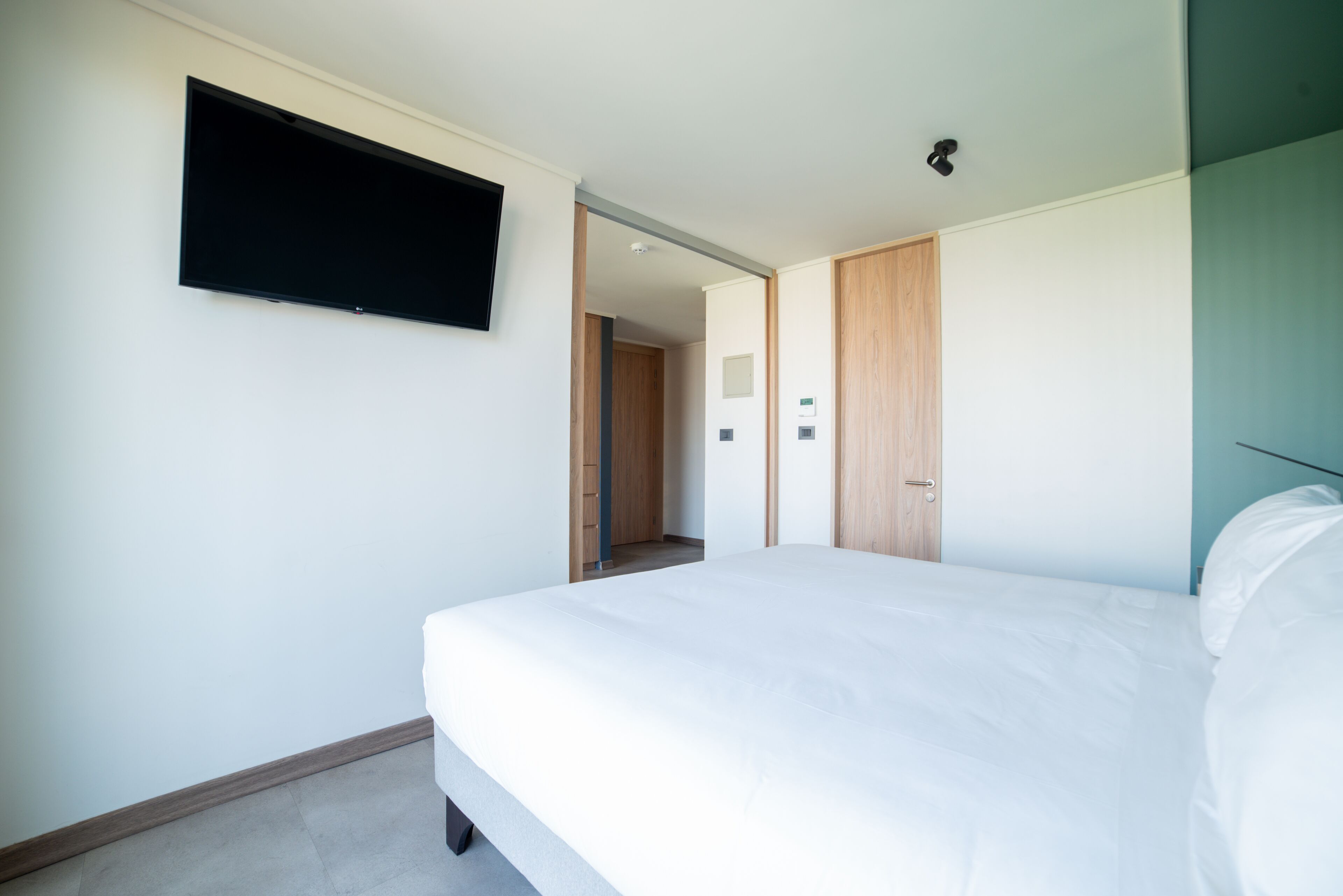 Una habitación de hotel moderna con una cama grande, un televisor de pantalla plana montado en la pared y un armario de madera.