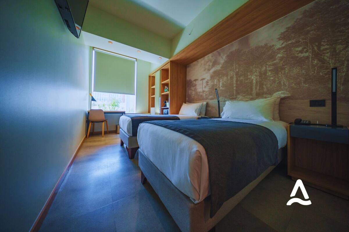 Een moderne hotelkamer met twee bedden, een bureau en een groot raam.