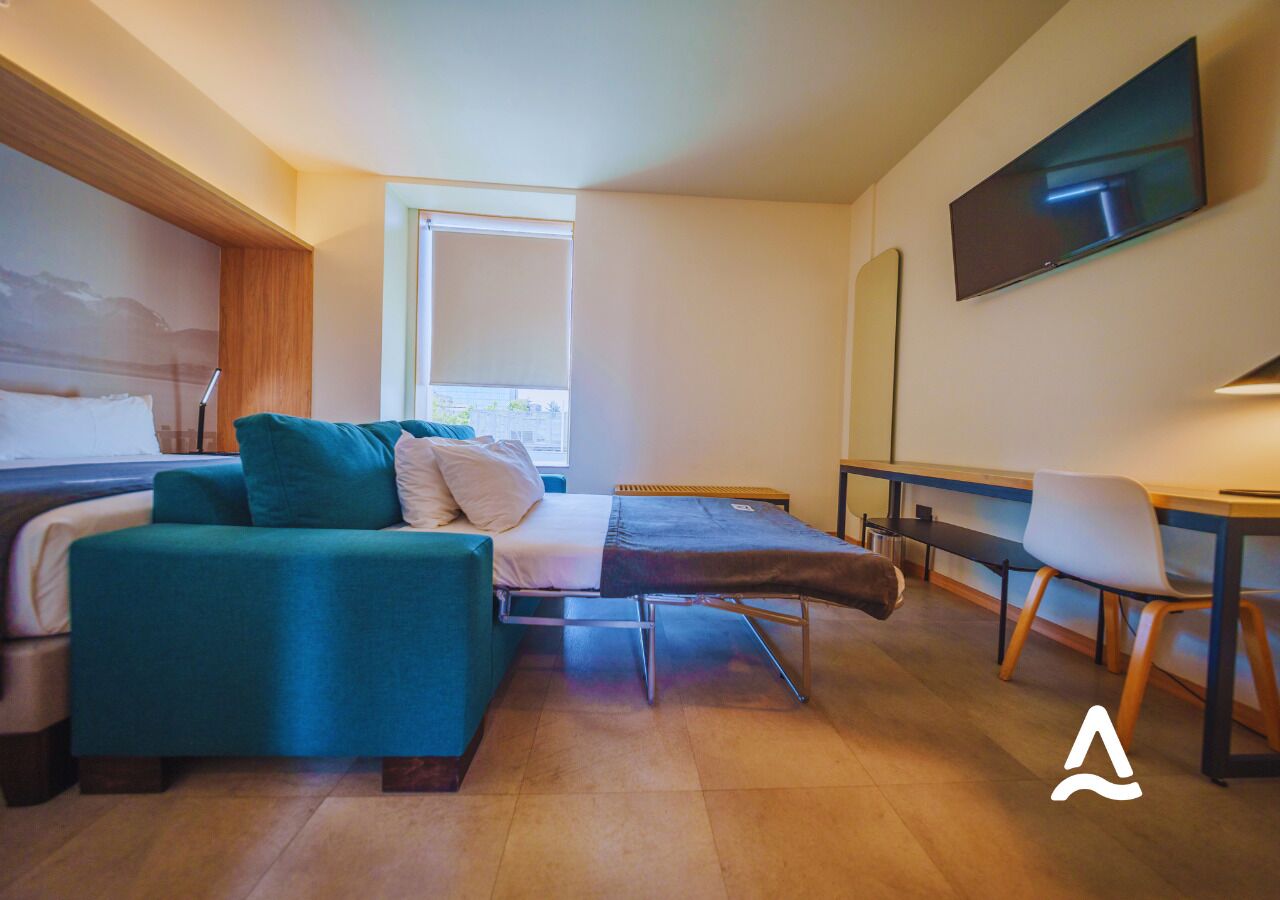 A modern hotel room with a sofa, a bed, a desk, and a TV.