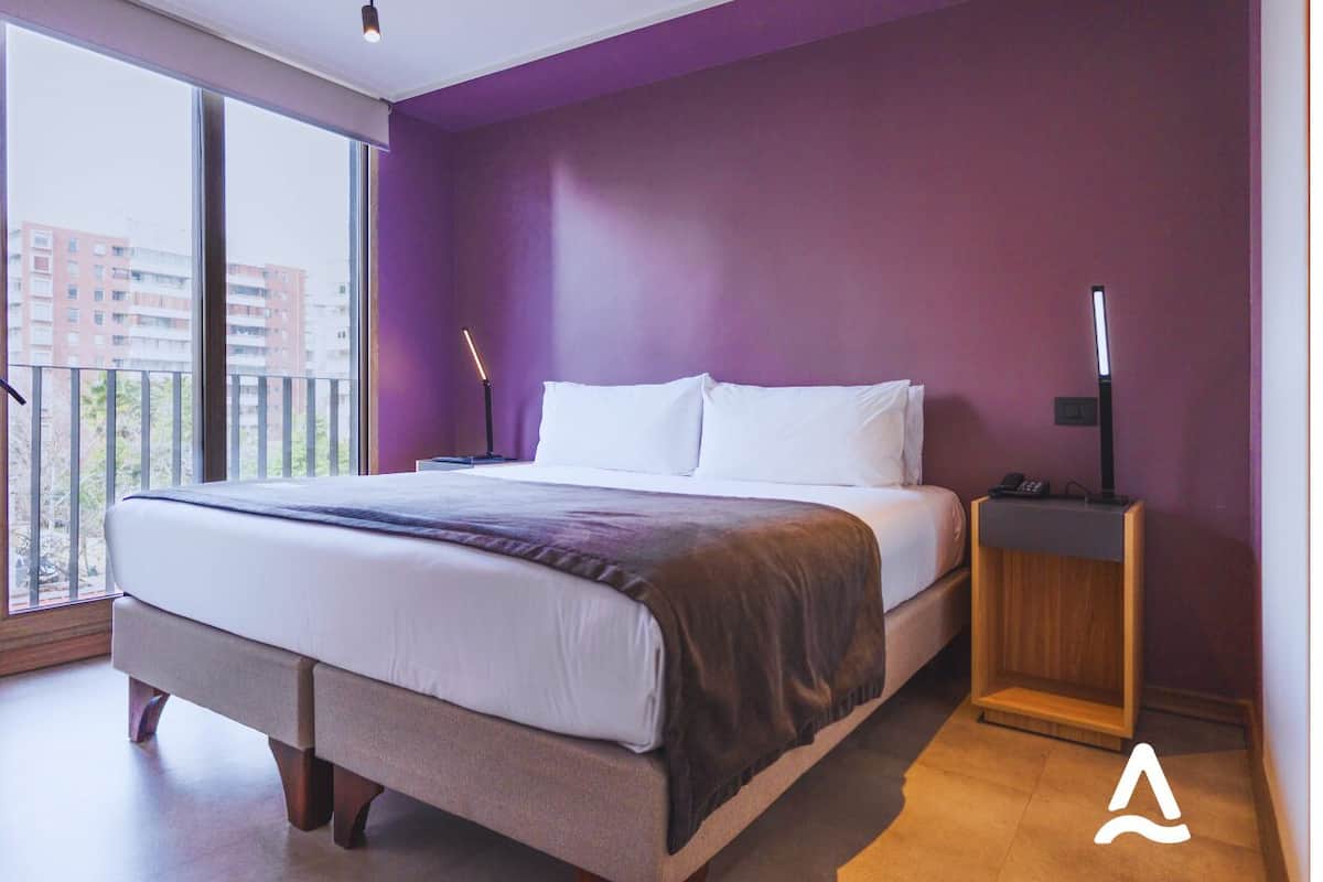Een moderne slaapkamer met een groot bed, een nachtkastje en uitzicht op de stad door grote ramen.