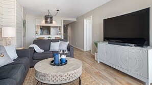 Una sala de estar moderna con un sofá gris, una mesa de centro redonda y un televisor de pantalla plana sobre un mueble blanco.