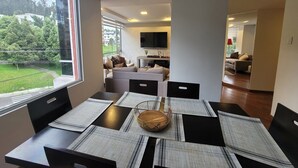 A modern dining area with a large window, a flat-screen TV, and a cozy seating area with a sofa and a coffee table. - 500 Excellent panoramic view, olympic stadium, park, mountain swimming pool (Quito)