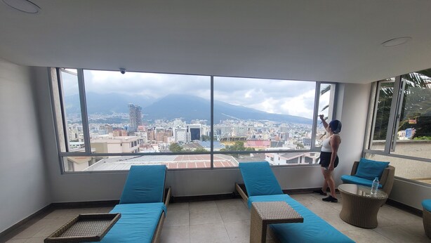A balcony with wicker lounge chairs and a large window offering a city view. - 500 Excellent panoramic view, olympic stadium, park, mountain swimming pool (Quito)