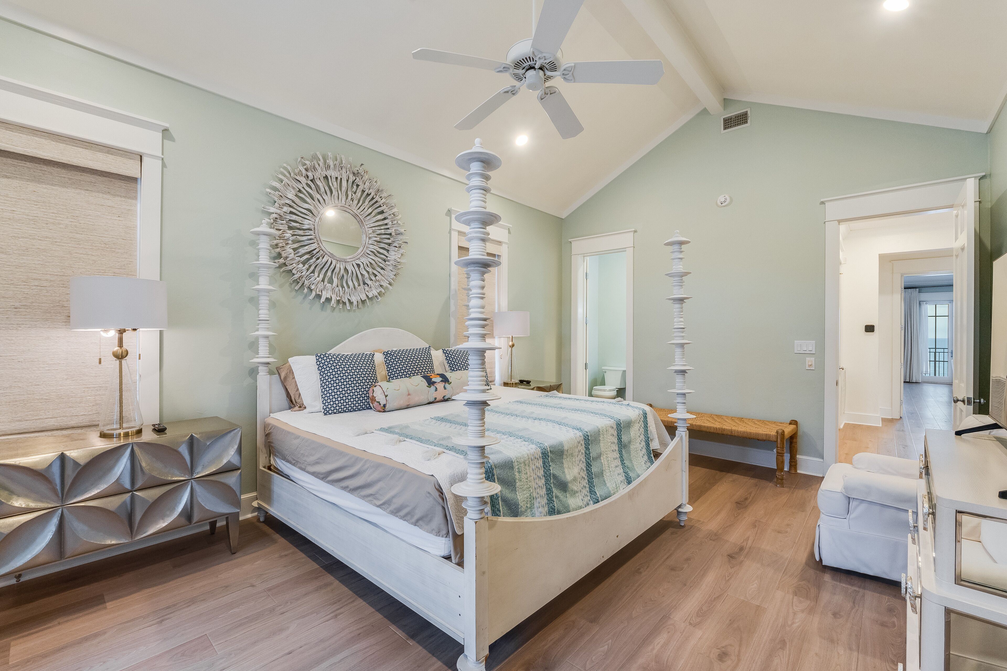 A bedroom with a bed, bedside tables, a ceiling fan, a mirror, and a door leading to another room.