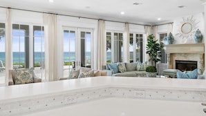 Un vaste salon agrémenté d’une grande table basse en marbre blanc, d’une cheminée et offrant une vue sur l’océan grâce à de larges fenêtres.