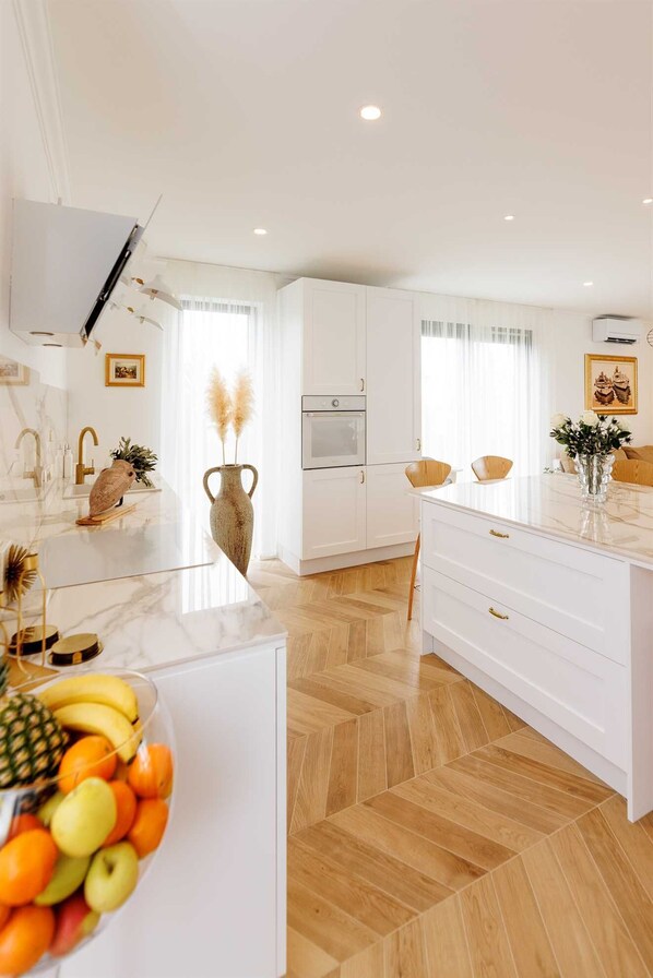Una cocina moderna con armarios blancos, una isla central con frutero y un suelo de madera en patrón de espiga.