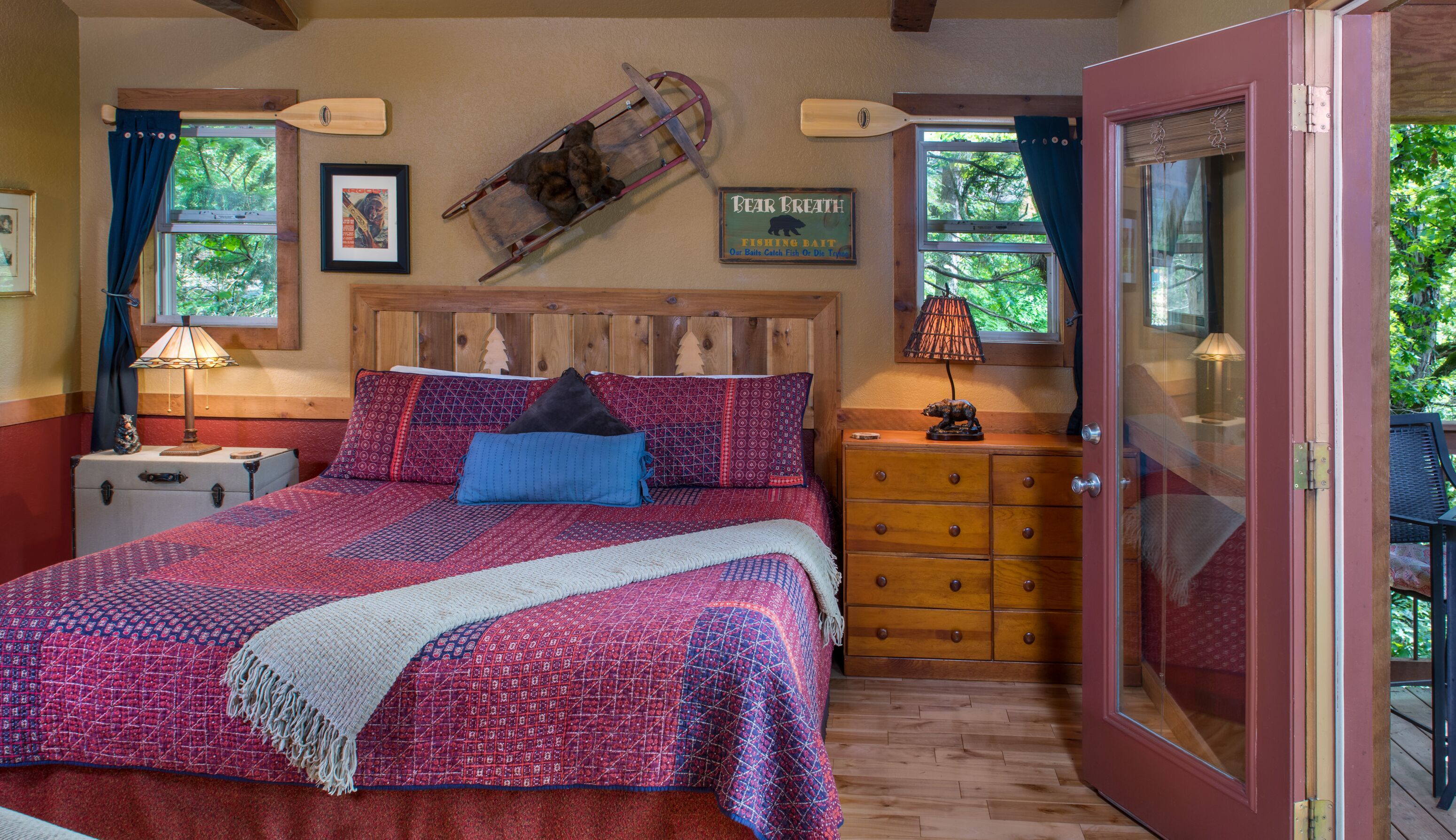 A cozy bedroom with a large bed, a dresser, a nightstand, a lamp, and a window with curtains.
