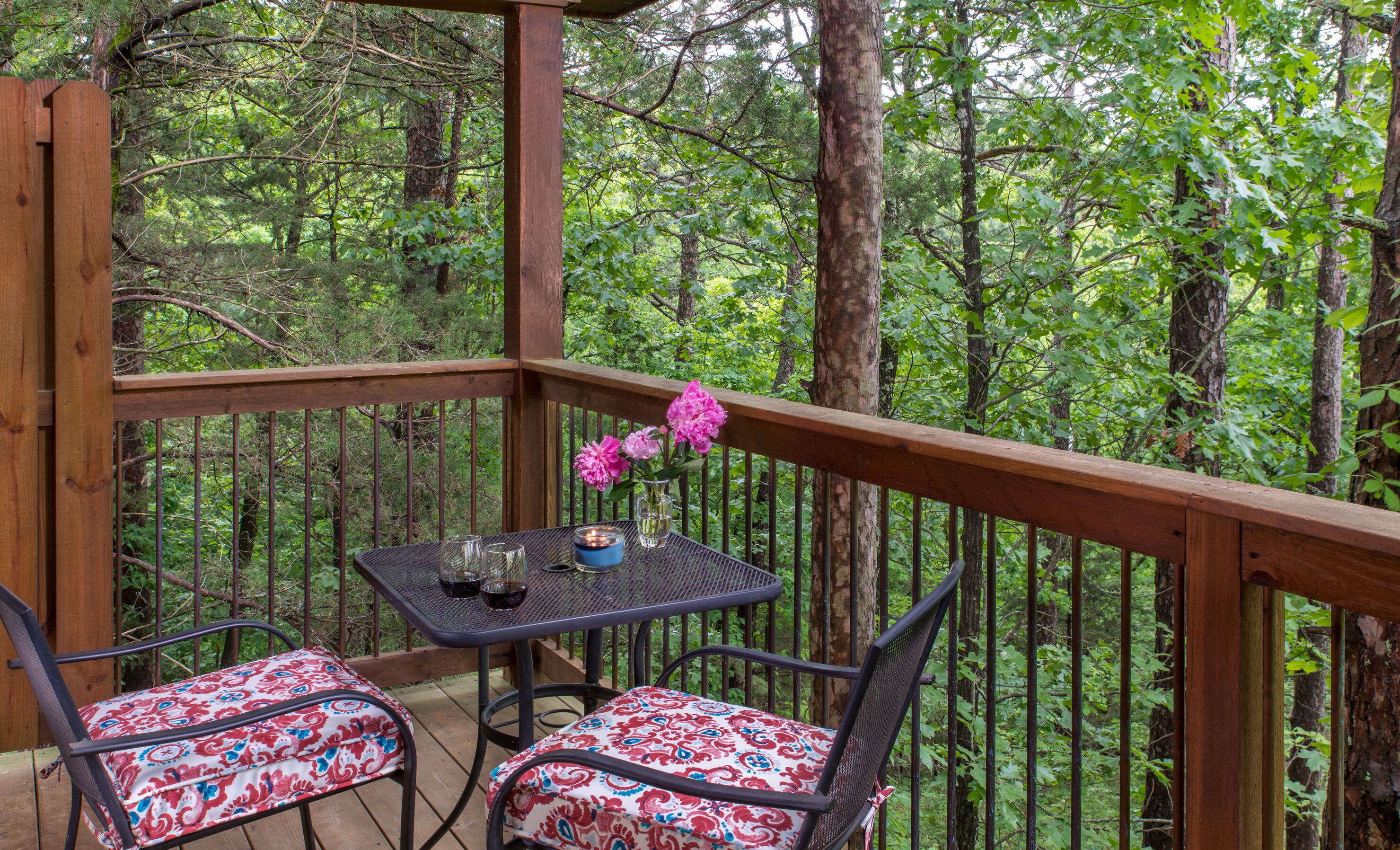 A wooden deck with two chairs and a table, surrounded by a forest.