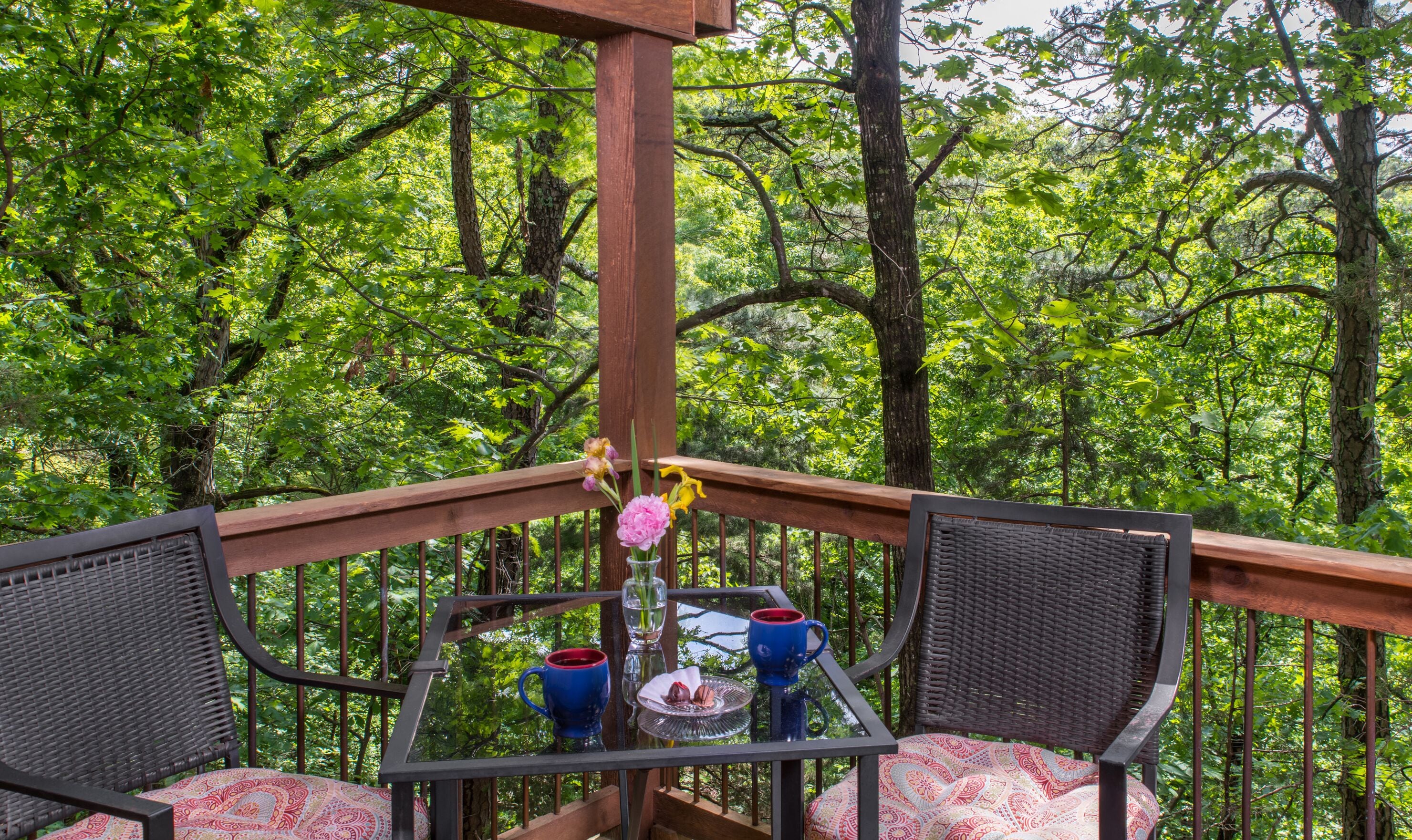 Een balkon met rieten meubilair, een glazen tafel en een vaas met bloemen.
