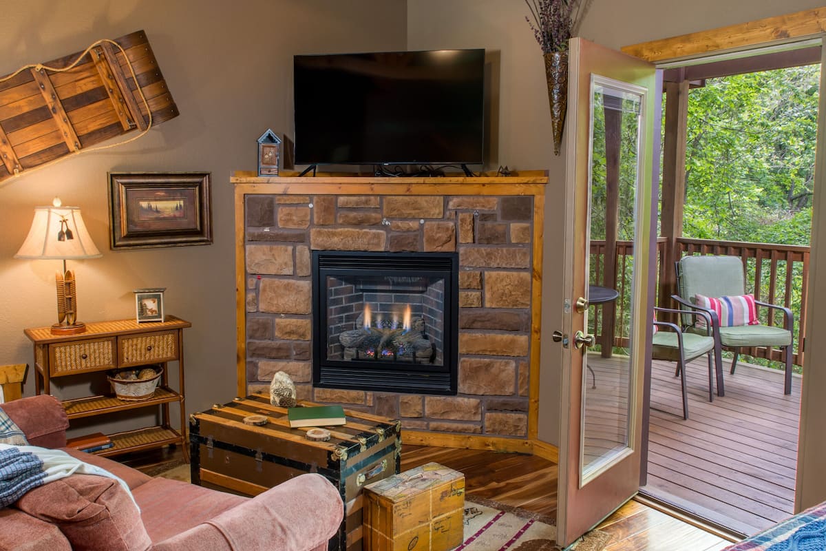 A cozy living room with a fireplace, a television, and a view of a wooden deck.