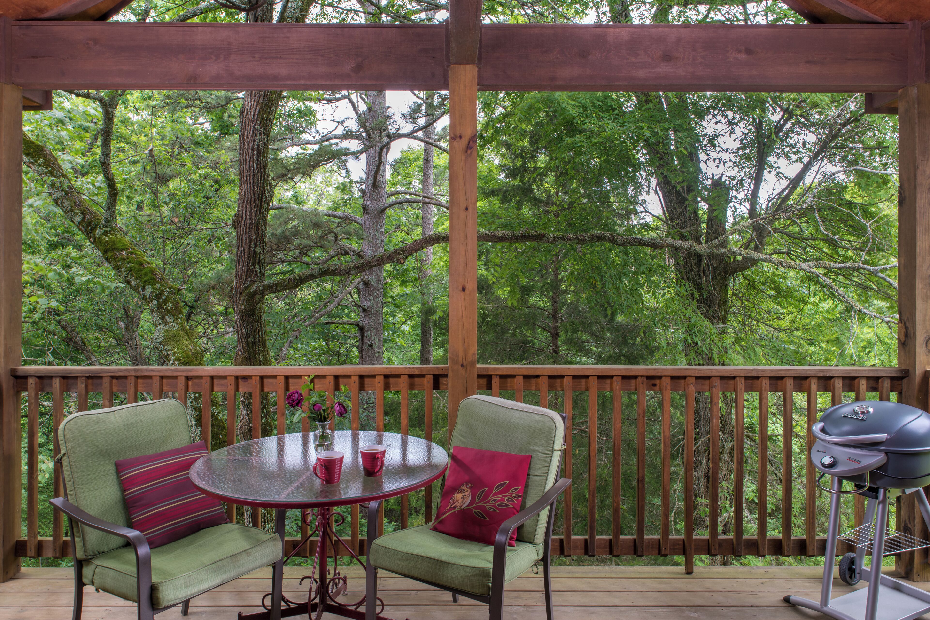 A covered outdoor area with two green chairs, a round table, and a grill.
