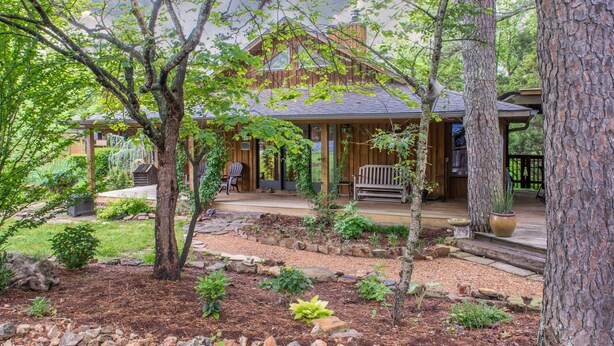A wooden cabin with a covered porch, stone pathways, and a garden with various plants. - Eureka Sunset Cabins (Eureka Springs)