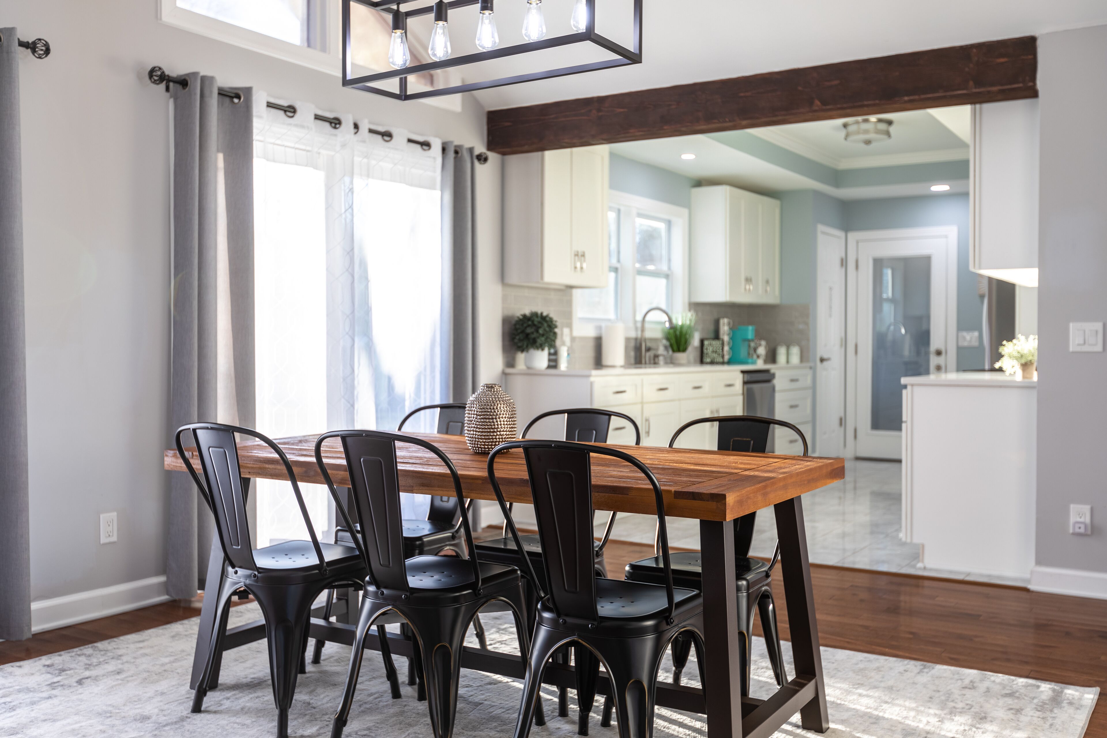 Un comedor con una mesa de madera y sillas negras, una cocina al fondo, y vista del comedor a través de un puerta abierta.