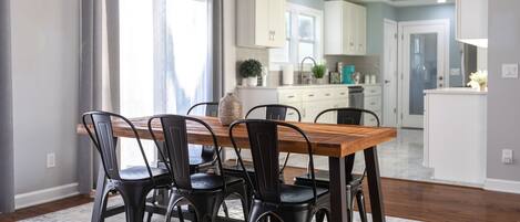 Un comedor con una mesa de madera y sillas negras, una cocina al fondo, y vista del comedor a través de un puerta abierta.