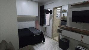 Une chambre à coucher de taille réduite, comprenant un lit, un petit canapé, une télévision et un miroir.