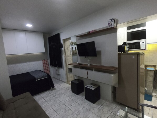 A compact room with a bed, a TV mounted on the wall, a microwave, and a small refrigerator.