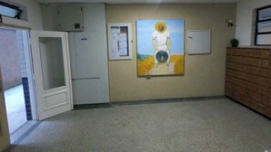 Un couloir avec un tableau représentant une figure sur un piédestal, une porte et un meuble.