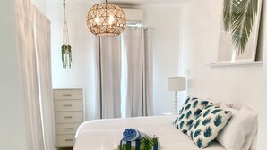 A bedroom with a bed, a hanging light fixture, a nightstand, and a wall-mounted air conditioner. - Alpha @Serendip Vacation Condos (Cruz Bay)