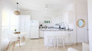 A modern kitchen with white cabinetry, a round dining table, and bar stools. - Alpha @Serendip Vacation Condos (Cruz Bay)