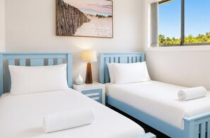 A hotel room with two beds, a nightstand with a lamp, a beach-themed wall art, and a window with a view of greenery. - Beachside Beauty - Short walk to Caves Beach (Caves Beach)