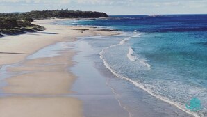 A beach with clear blue water, sandy shore, and a distant rocky outcrop. - Beachside Beauty - Short walk to Caves Beach (Caves Beach)