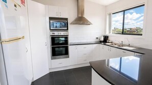 A modern kitchen with white cabinets, a stainless steel range hood, a built-in oven, and a large window. - Beachside Beauty - Short walk to Caves Beach (Caves Beach)