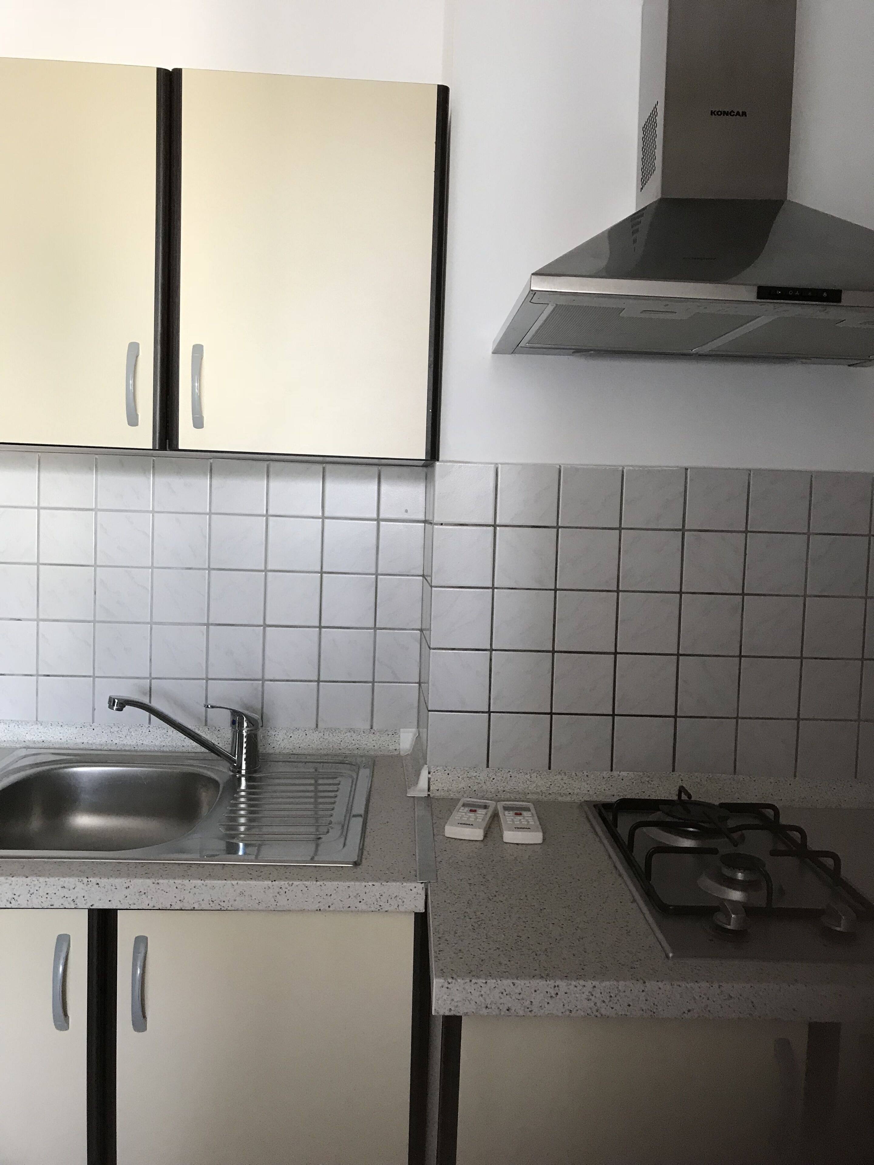 Una cocina con gabinetes blancos, un lavamanos de acero inoxidable, una estufa a gas y una campana extractora.