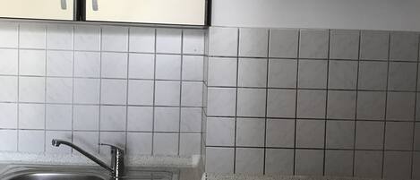 Una cocina con gabinetes blancos, un lavamanos de acero inoxidable, una estufa a gas y una campana extractora.