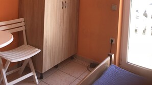 A small room with an orange wall, a wooden wardrobe, a white chair, a small table, and a window with a view. - 5 minutes from the amusement park (Privlaka)