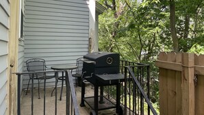Een terras met een barbecue, stoelen en een tafel.