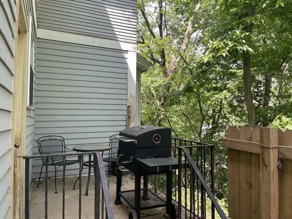 Een terras met een barbecue, stoelen en een tafel.