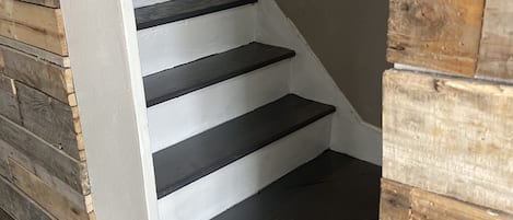 Una escalera con escalones negros y paredes blancas que conduce a un muro de madera.