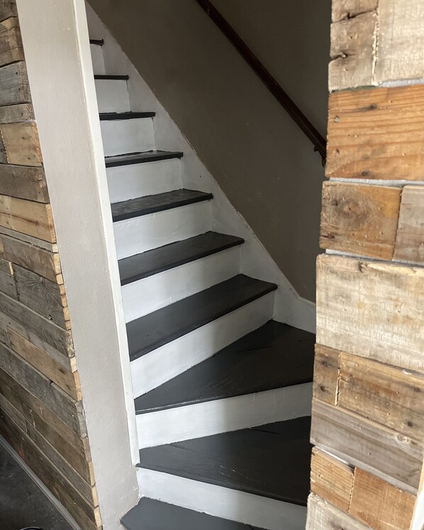 A staircase with black steps and white walls, leading to a wooden wall.