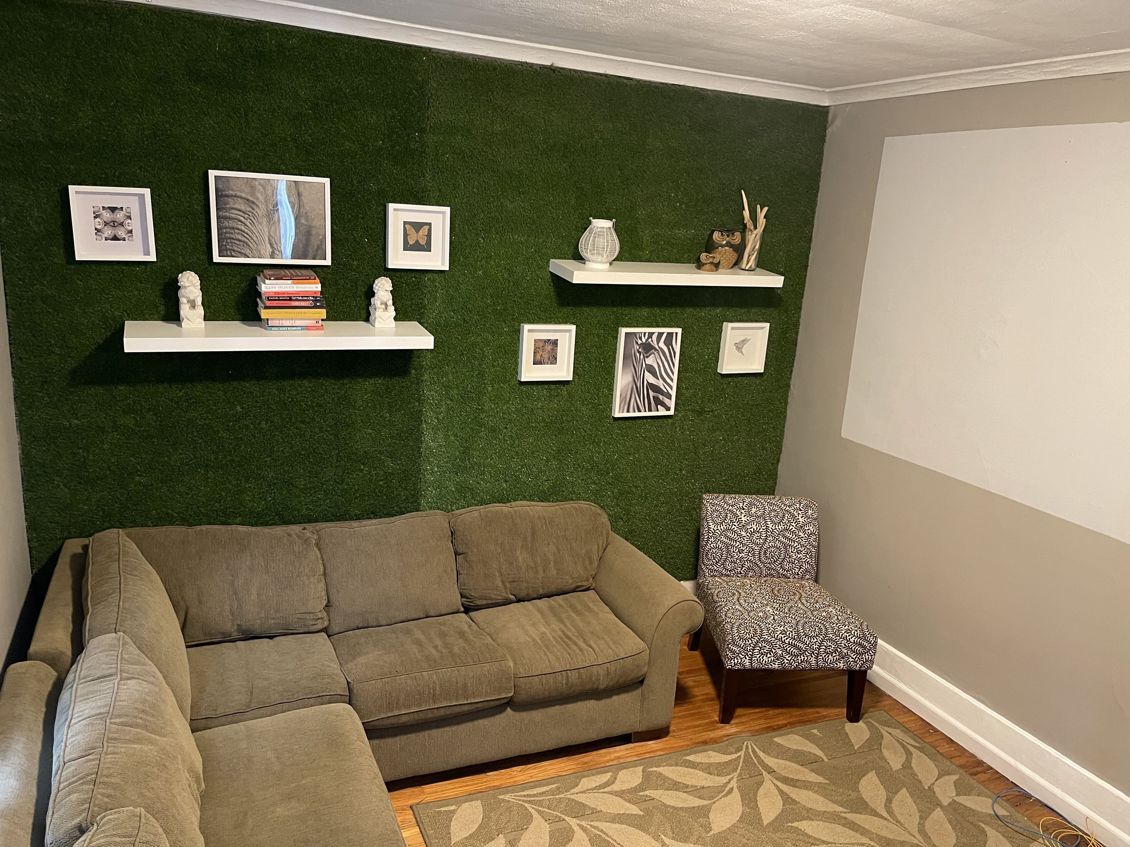 Un salon avec un mur vert, un canapé, un fauteuil et des étagères ornées de tableaux et de livres.