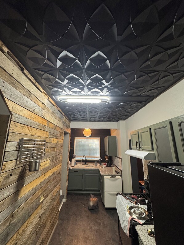 Een compacte keuken met een houten wand, een modern plafond en een klein raam met zonwering.