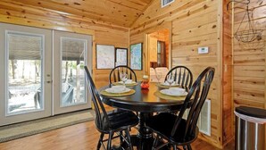 Una sala da pranzo in una baita di legno con un tavolo rotondo apparecchiato per quattro persone, sedie e vista attraverso la porta vetrata.