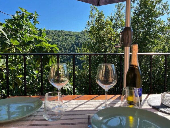 Mesa al aire libre con una botella y vasos, con vistas a una ladera boscosa.