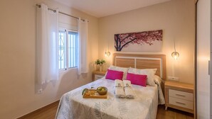 Ein ordentlich gemachtes Bett mit Blumenmuster, zwei rosafarbene Kissen und einem Tablett mit Früchten und Handtüchern.